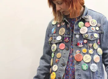A young woman wearing a denim jacket covered in badges