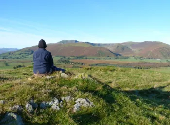 A person sitting on a rock looking towards a hill called Blencathra 