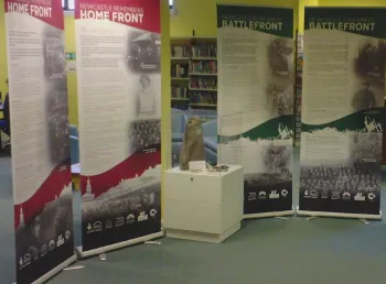 A woman stands by four pull up displays, a model uniform on a mannequin and a glass case containing replica first world war objects