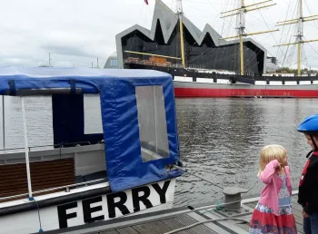 A boy and a girl, stand facing each other on a waterfront near Glasgows Riverside Museum
