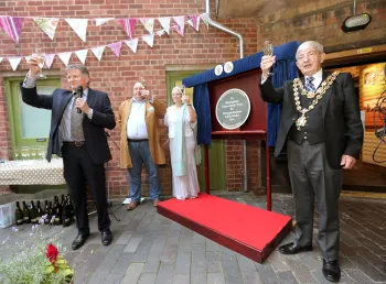 A group of people holding glasses gathered around an unveilled plaque