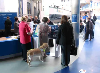 A visitor accompanied by a guide dog uses braille signage