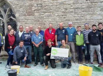 A group of people with gloves and buckets standing in front of a church wall