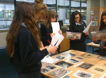 A group of young women standing around a table covered in old photographs