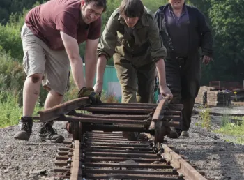 Two teenage trainees lay a new railway track by hand supervised by an older volunteer