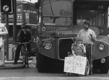 An archive image showing a person in a wheelchair holding a sign in front a double double bus. There is a police officer on the left hand side.