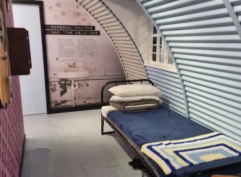 A reconstructed prison cell inside a Nissen hut containing a bed and a guitar