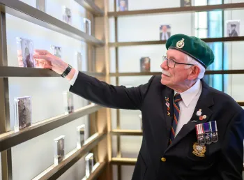 A vetaran wearing a green beret looks at black and white photographs of people in an exhibition space