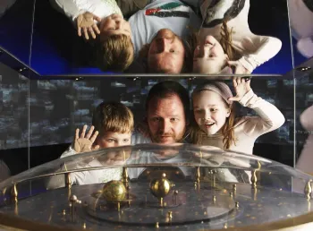 A man and two children look at a machine of an Earth spinning around the sun at the Royal Observatory Greenwich