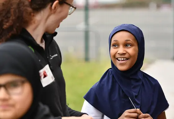 An adult talks to a child wearing a head scarf.