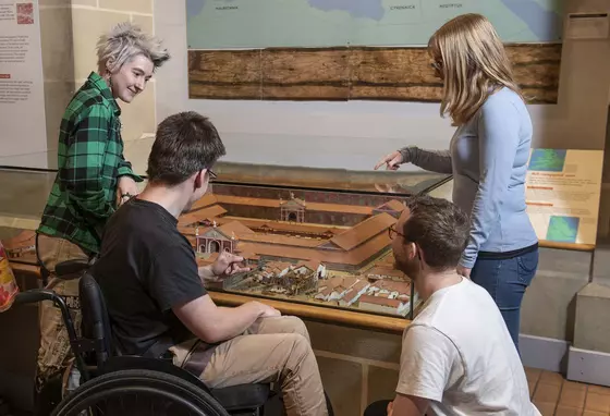 Four young people chatting and looking at a display of a small historical model settlement
