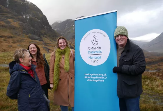 People posing with the Heritage Fund logo with a beautiful landscape of a glen in the background
