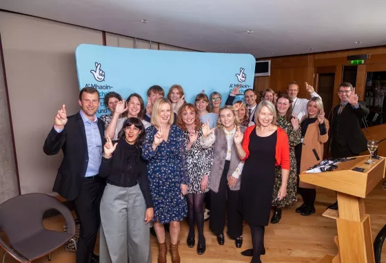 A group of people at an event crossing their fingers to match The National Lottery logo