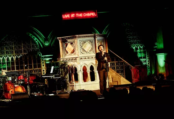 Nish Kumar performing at Union Chapel in front of pulpit and Live at the chapel LED sign