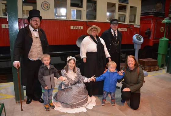 People in period costumes with children in front of an old train