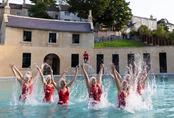 A group of swimmers in red swimsuits jumping out of the water at Cleveland Pools