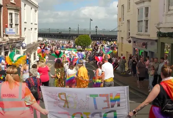 People wear colourful clothes and hold banners and rainbow flags at Isle of Wight Pride.