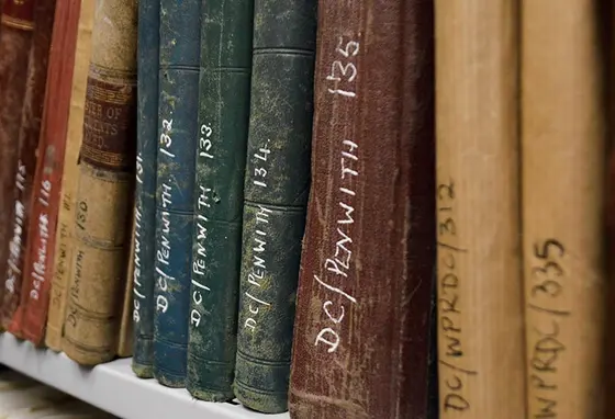 A bookshelf of old books in an archive. The books have reference numbers written on their spines.