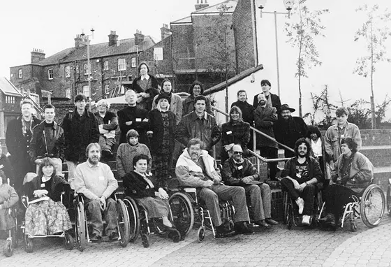 A black and white group photo of about 30 people. The front row of people are using wheelchairs, with others standing on steps behind them.