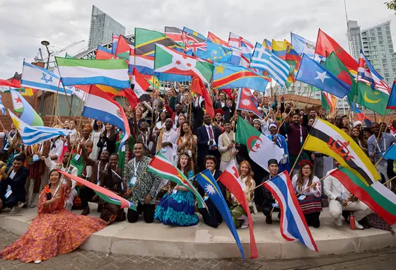 A large group of people sitting on a roundabout all holding flags for different countries of the world
