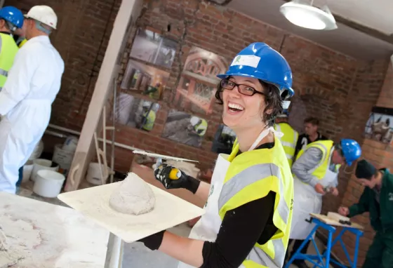 A smiling woman holding a board with plaster on it and a trowel