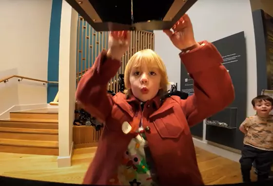 A young boy opening a box at a museum with a 'wow' expression on his face