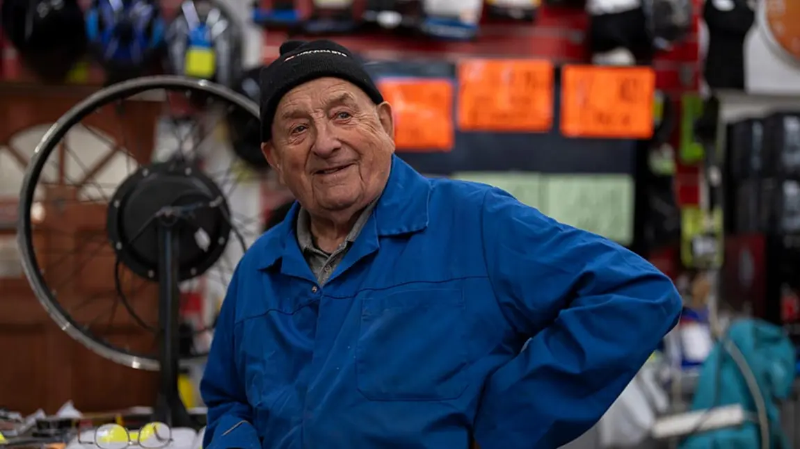 an older man wearing blue overalls in a bicycle repair shop