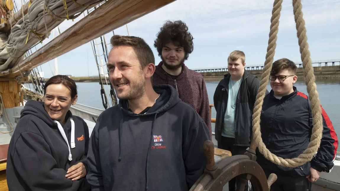 A group of young people standing on deck of a tall ship in dock.