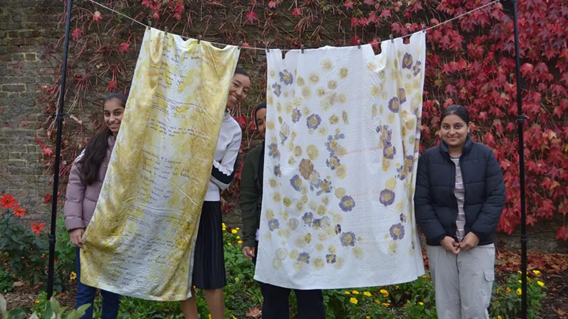 People standing behind a textile artwork made from hanging sheets of fabric printed with text and flowers
