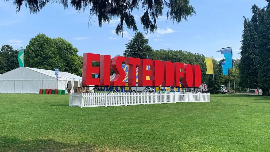 Large red letters spelling ‘Eisteddfod’ in front of tents in a field