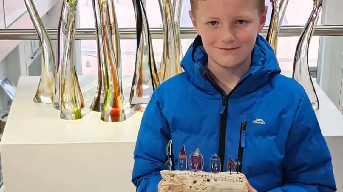 A young person holds their artwork as part of the exhibition.