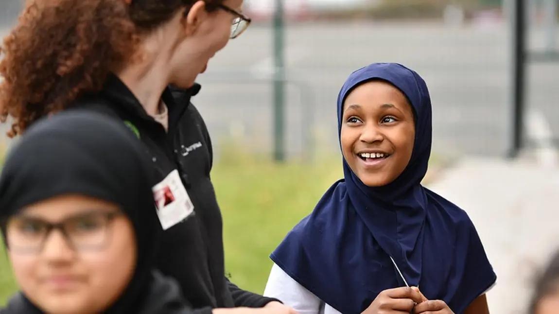 An adult talks to a child wearing a head scarf.