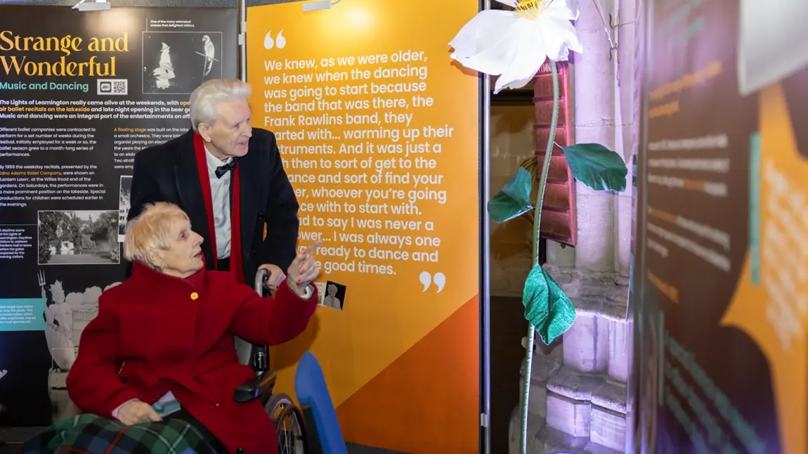 An elderly couple, smartly dressed, explore the exhibition displays together.