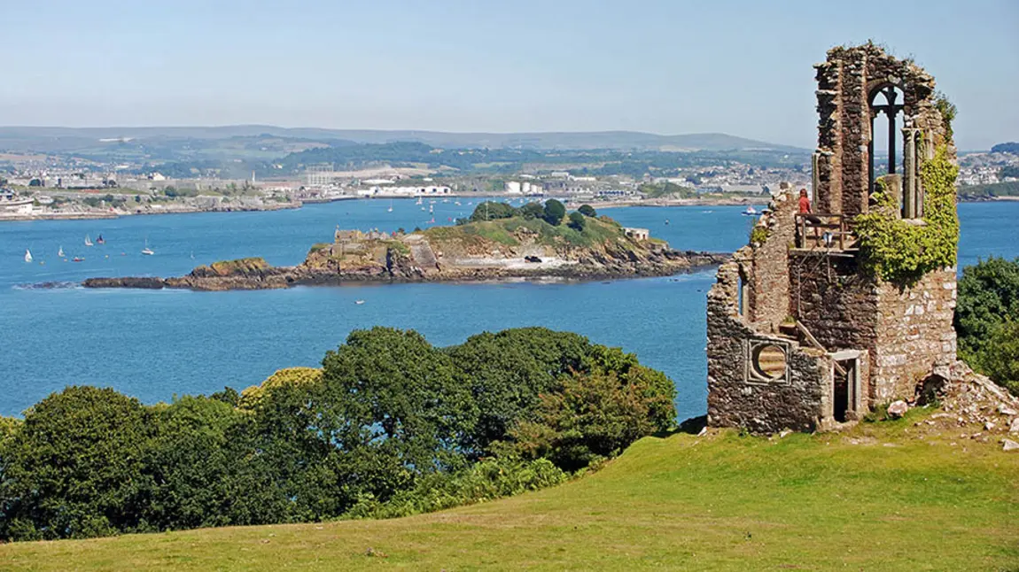 A ruined folly with a coastal landscape during summer in the background