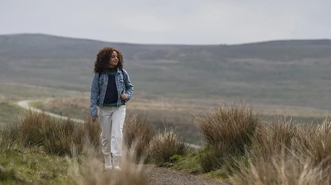 A young woman walks through a moorland landscape