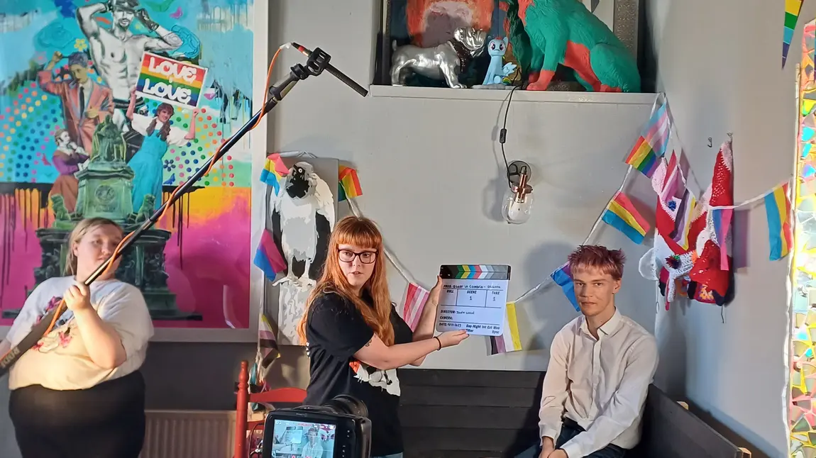 Three young people making a film, one person is holding a microphone, another a clapperboard, and one person is waiting to be interviewed