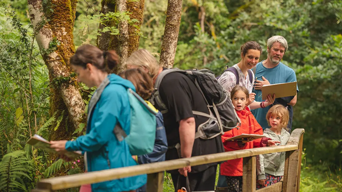 A mix of adults and children wearing outdoor clothes in a forest
