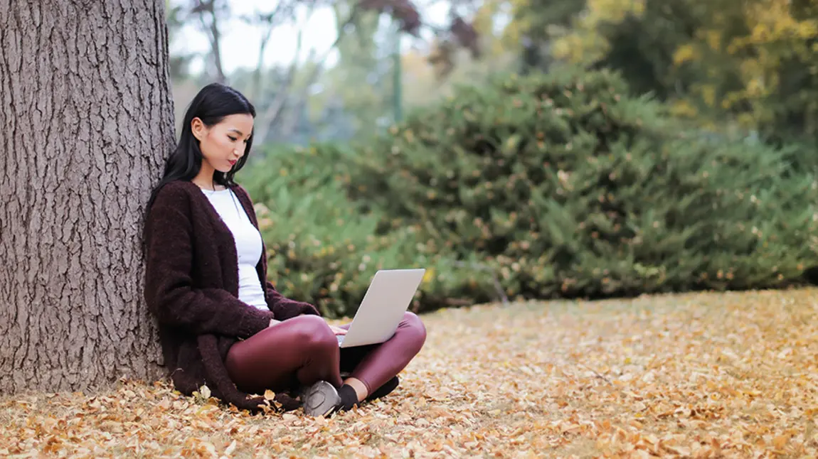 A young woman using a computer laptop under a tree
