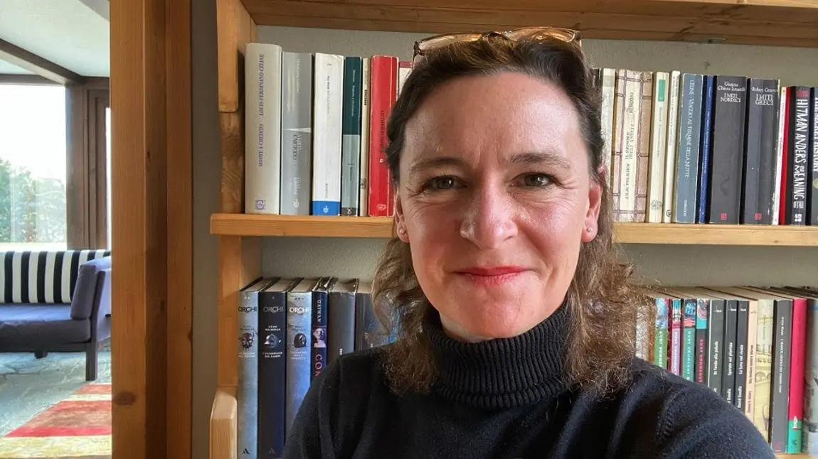 Caroline Crewe-Read A woman in a black polo neck jumper standing in front of a bookshel