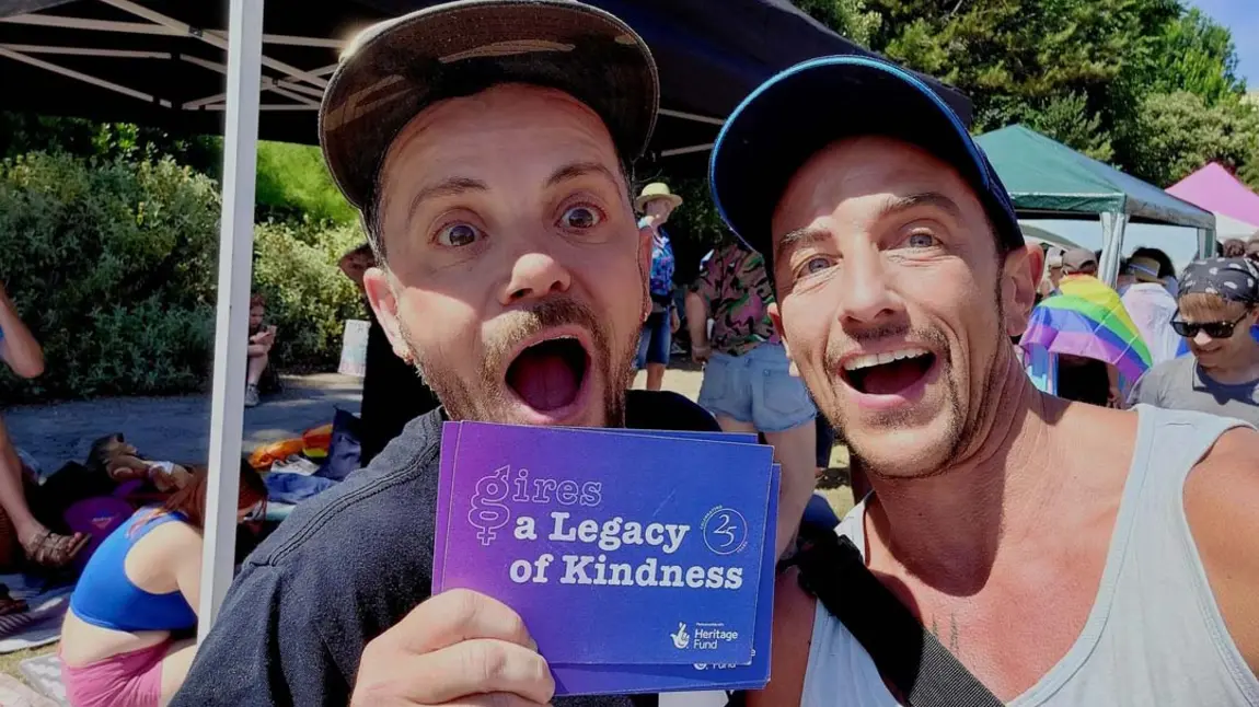 Two people at an outdoor event holding a card saying A Legacy of Kindness