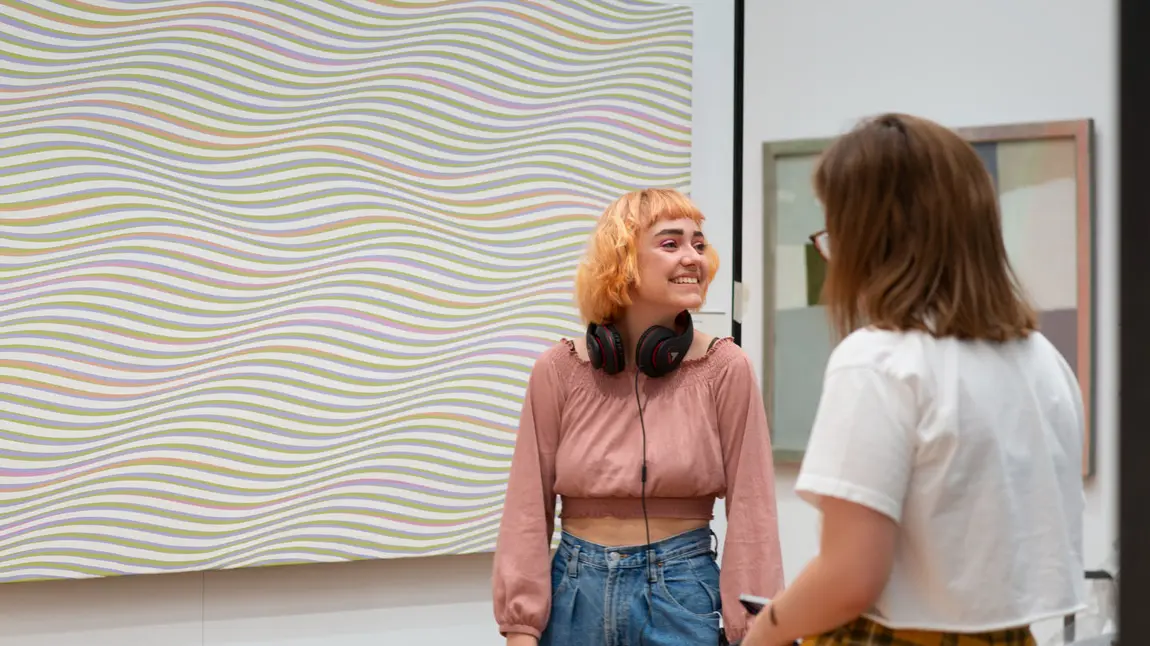 Two Gallery visitors in front of a Bridget Riley patterned painting