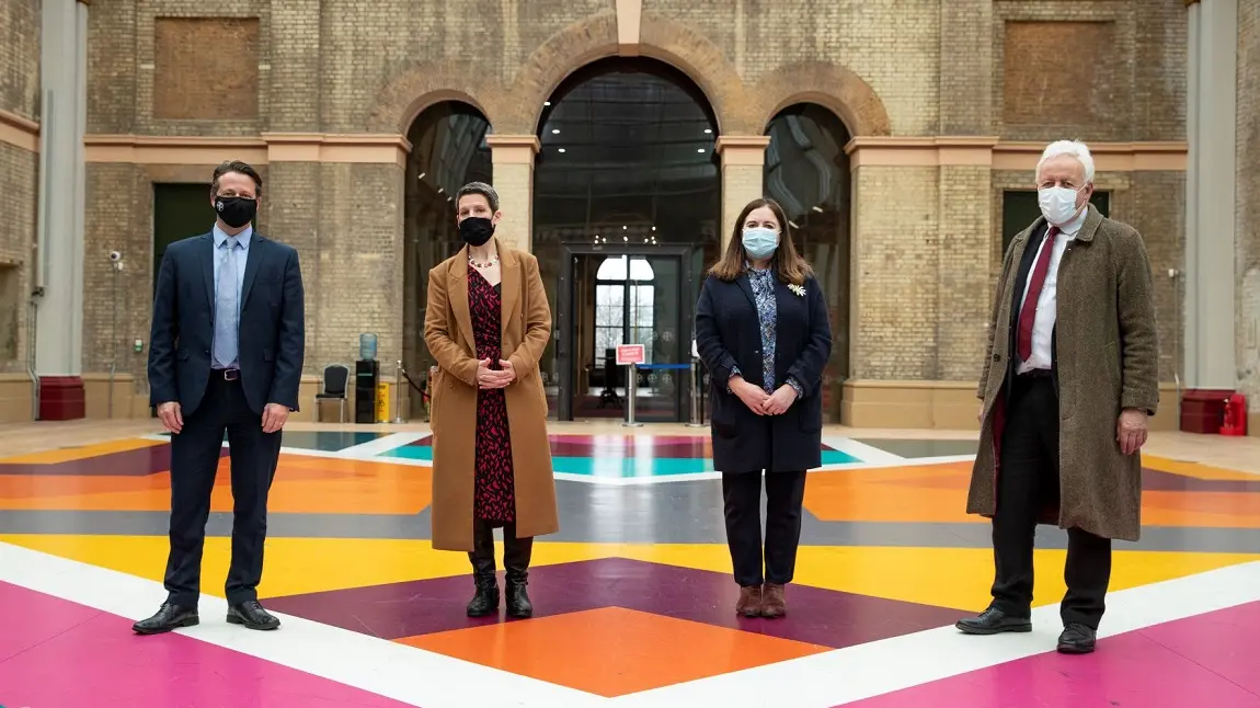 Four people standing inside Alexandra Palace, socially distanced with masks on