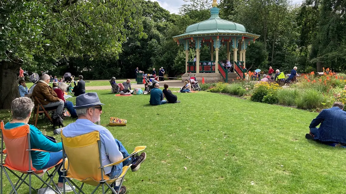 People sitting in a sunny park, near a bandstand