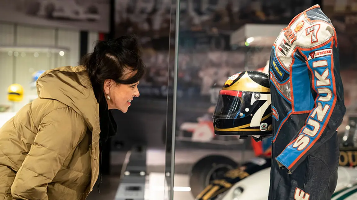 Woman looking into a glass case displaying Barry Sheene's racing leathers and helmet
