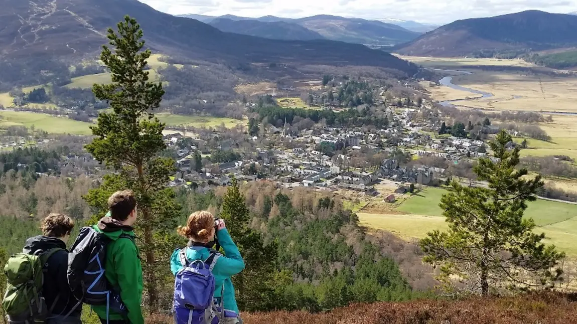 Three people look down over a valley with mountains in the distance