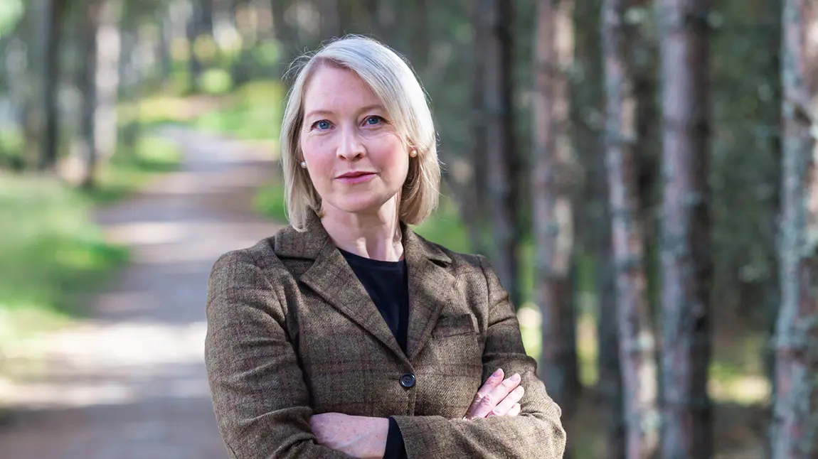 Person stands in nature with arms crossed, looking at camera