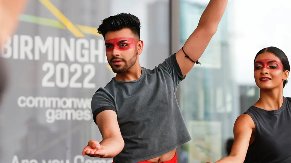 Two people striking a dance pose in front of a 'Commonwealth Games' sign 