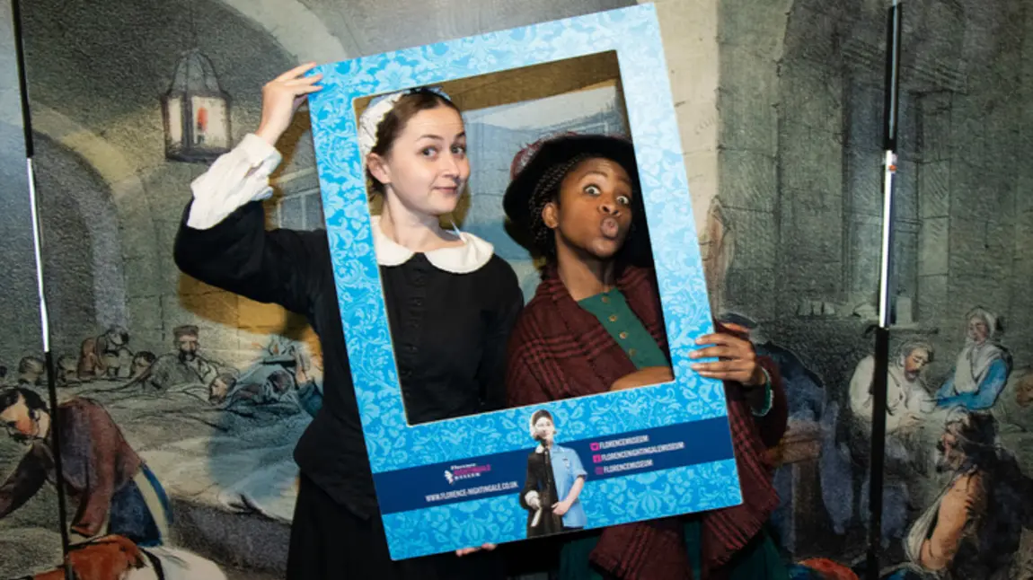 Image of two people in historic nursing outfits depicting Mary Seacole and Florence Nightingale, holding a frame to their faces
