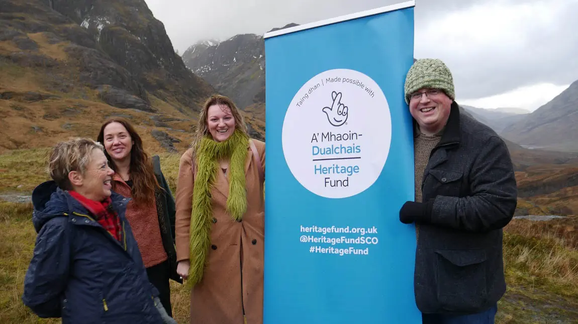 People posing with the Heritage Fund logo with a beautiful landscape of a glen in the background