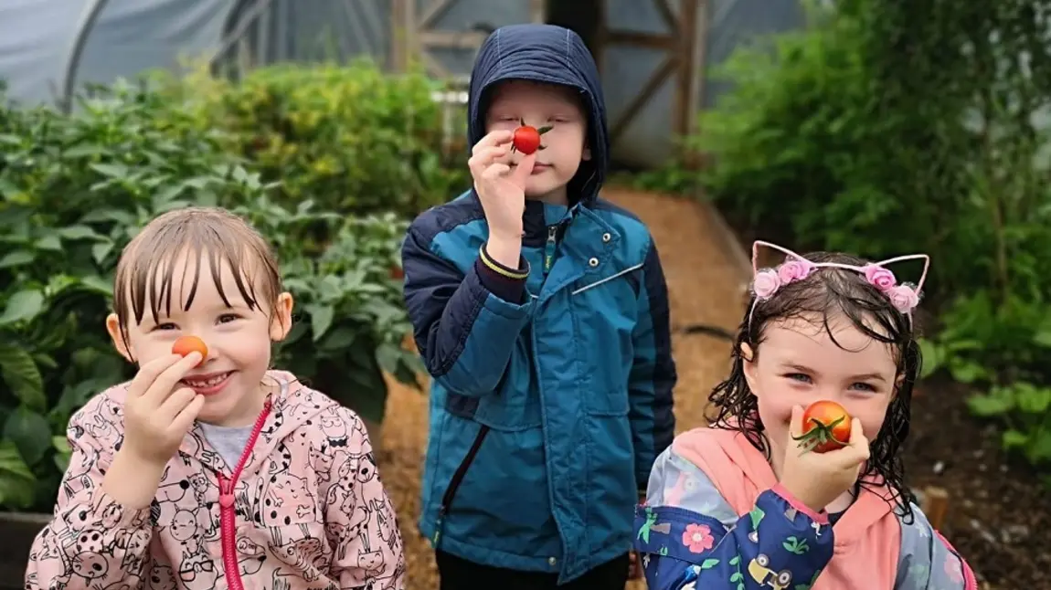 Three children hold tomatoes to their noses